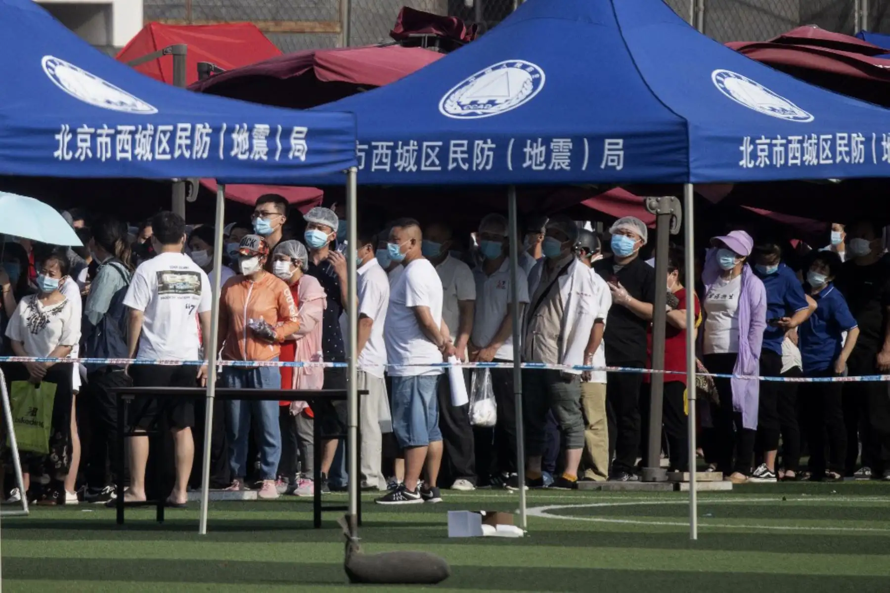 Las personas que viven cerca o han visitado el mercado Xinfadi, un mercado de alimentos al por mayor donde ha surgido un nuevo grupo de coronavirus  usan máscaras faciales mientras hacen cola para realizar pruebas en el centro deportivo de Guang