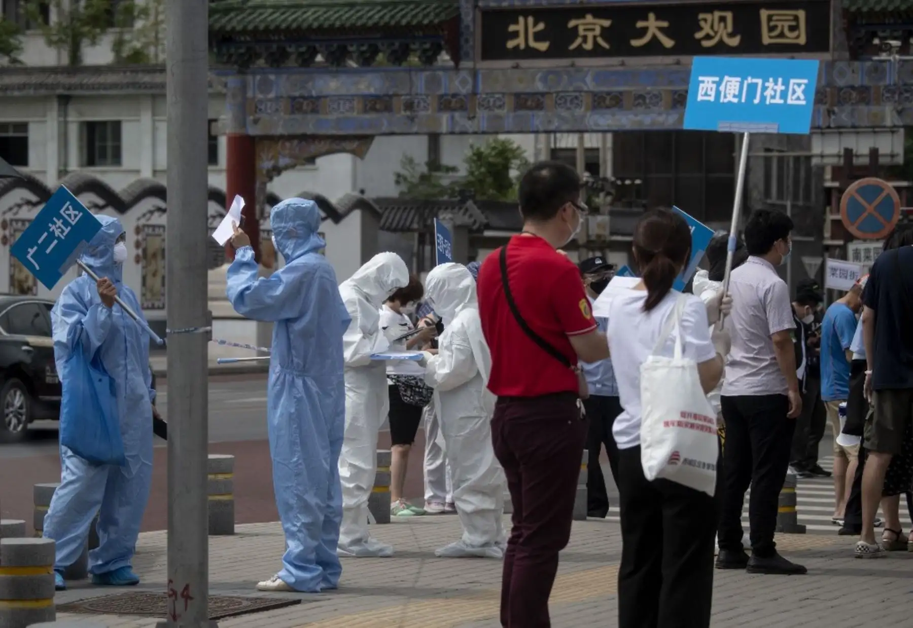 El personal médico con equipo de protección completo lleva carteles para ayudar a las personas que viven cerca o que han visitado el mercado Xinfadi, un mercado de alimentos al por mayor donde ha surgido un nuevo rebrote de coronavirus. Foto: AFP