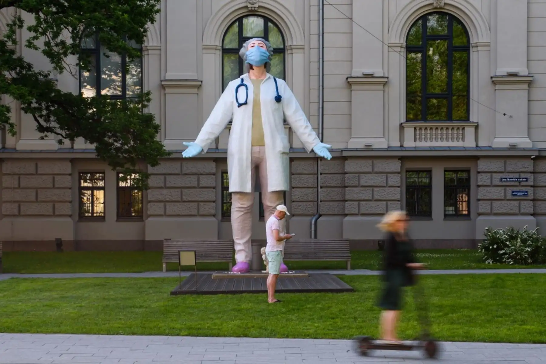 Una mujer en un scooter pasa junto a una estatua de una doctora de 6 metros de altura de la artista letona Aigars Bikse llamada "Medics to the World", que se encuentra frente al National Museum of Arts, en Letonia. Foto: AFP