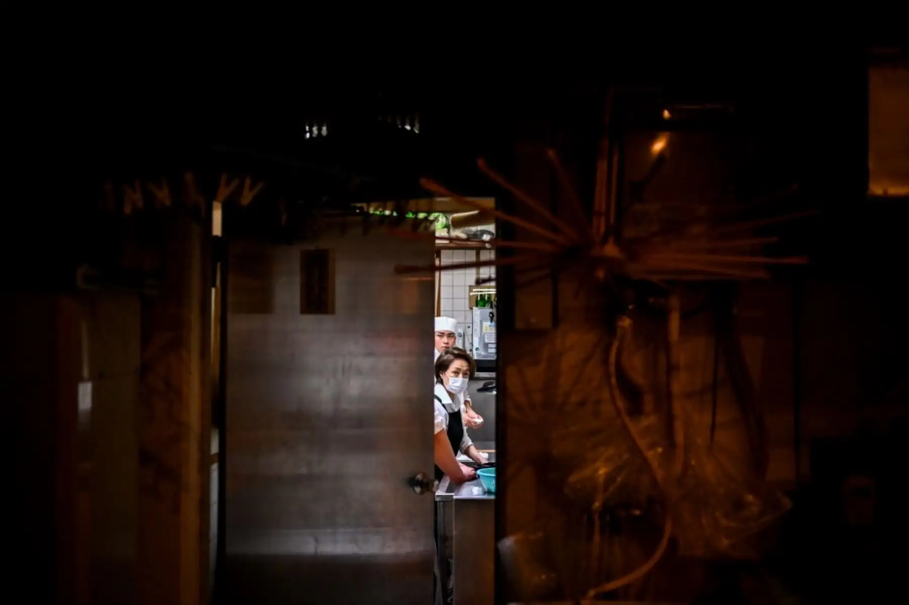 Dos cocineros con mascarillas observan desde la puerta del restaurante donde trabajan durante la noche, en Tokio. Foto: AFP