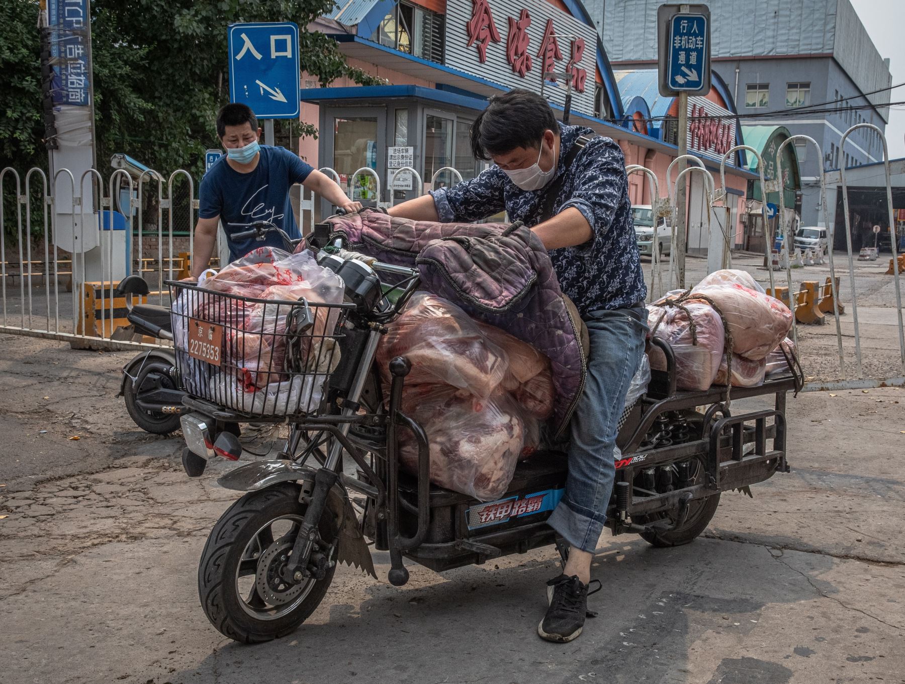 Hombres con máscaras protectoras cargan un scooter con carne al lado del edificio cerrado del mercado Xinfadi, en el distrito de Fengtai, Beijing, China. Uno de los mercados más grandes de Beijing, Xinfadi en el distrito de Fengtai. Foto: Efe.