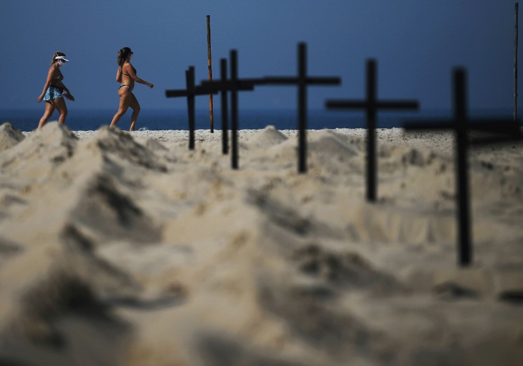 Los visitantes de la playa de Copacabana caminan frente a 100 tumbas simuladas, excavadas por activistas de la ONG brasileña Río de Paz, que simboliza las muertes por el covid-19. Foto: AFP