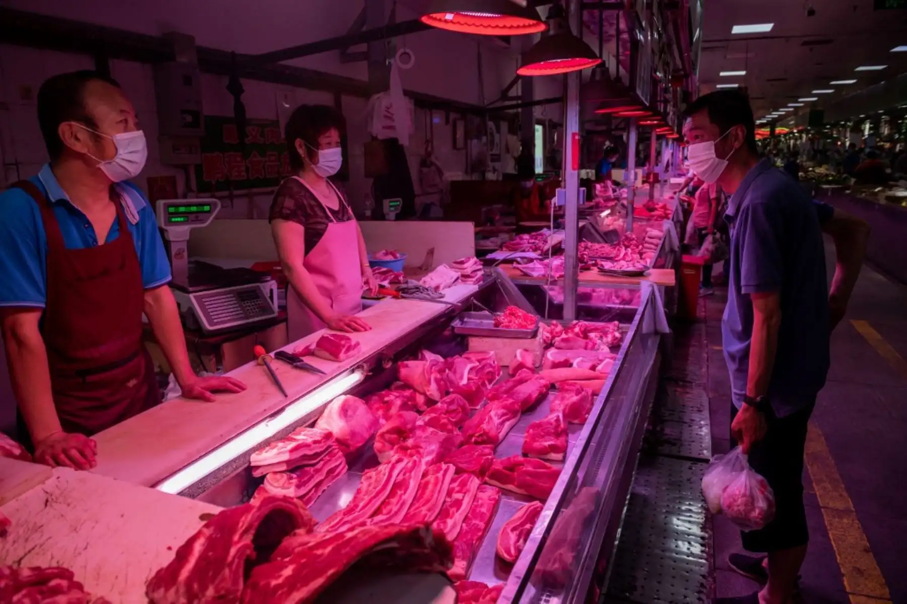 Un cliente habla con los carniceros después de que compró carne de su puesto en un mercado en Pekín. Foto: AFP