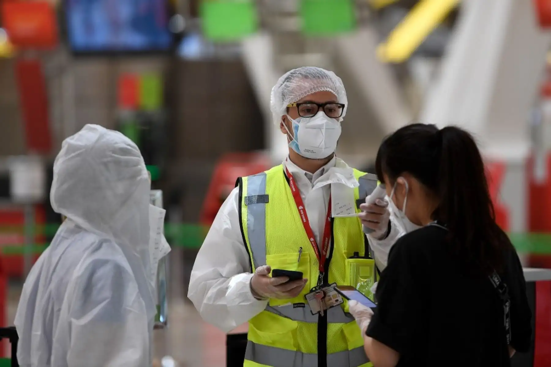 Un empleado con equipo de protección completo verifica la temperatura de los pasajeros que llegan para registrarse para su vuelo con destino a Pekín. Foto: AFP