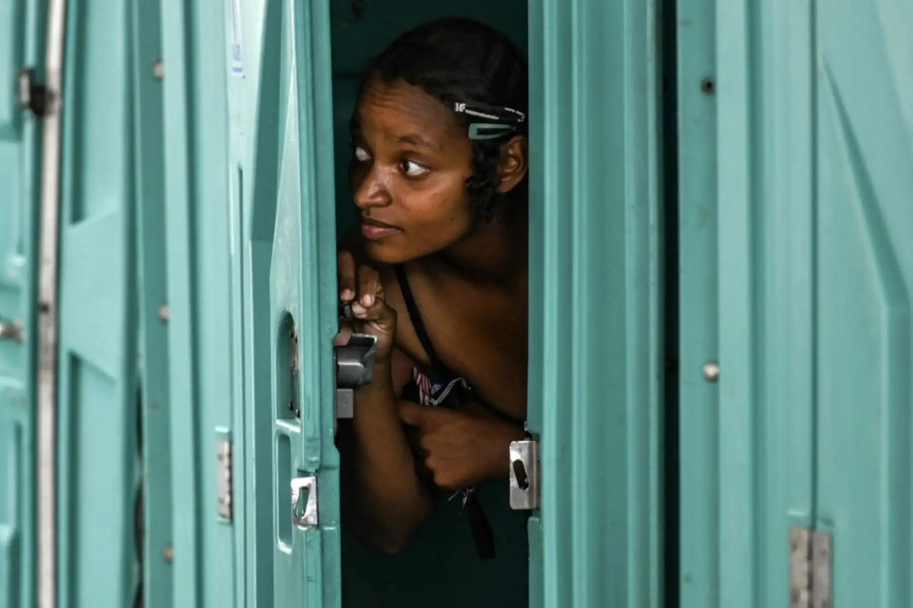 Una mujer mira por la puerta de la cabina de un baño químico antes de bañarse en un área provista para personas sin hogar para bañarse y comer en medio de la pandemia  en Medellín.
Foto: AFP