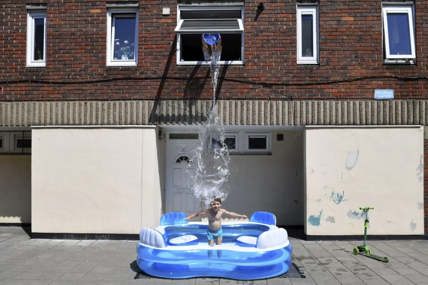 Kamila llena una piscina infantil arrojando agua desde una ventana de arriba sobre su hijo, Luca, de cinco años, mientras está parado en Hackney, al este de Londres.Foto:AFP