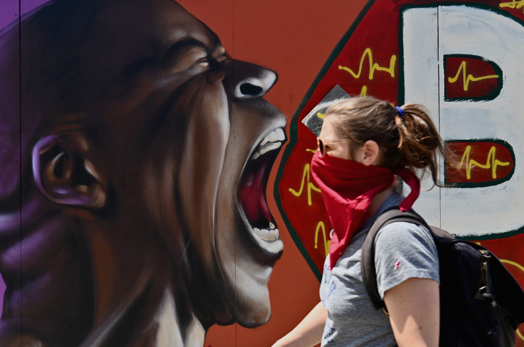 Una persona con mascarilla camina junto a un mural callejero en el distrito de Brooklyn de la ciudad de Nueva York. Foto: AFP