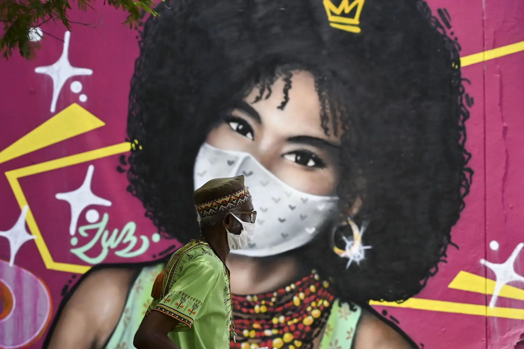 Un hombre usa una máscara facial como medida preventiva contra la propagación del nuevo coronavirus cuando pasa junto a un mural en Cali, Colombia. Foto: AFP