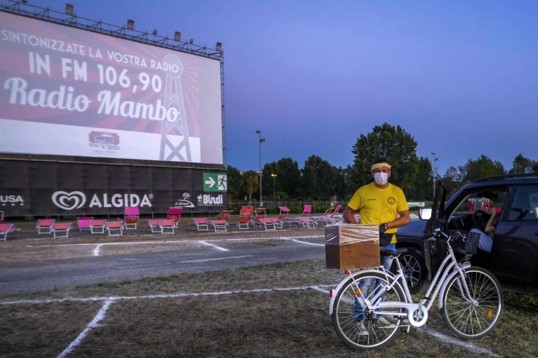 Un camarero en bicicleta entrega comida y bebidas a las personas que se preparan para ver desde su automóvil la comedia italiana "Tolo Tolo" dirigida por Checco Zalone en la noche de apertura del mayor autocine 