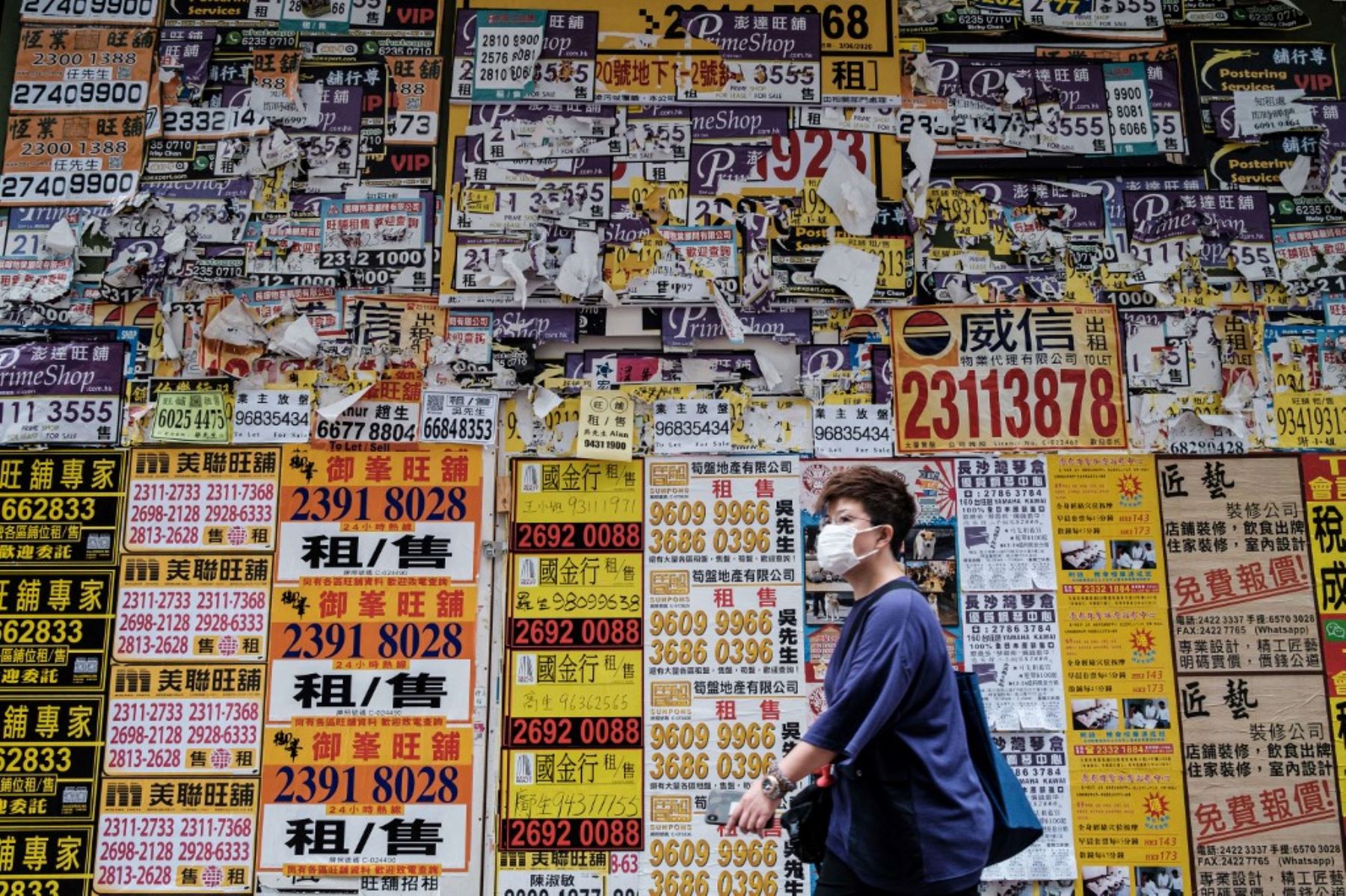 Un peatón camina junto a una tienda cerrada repleta de carteles publicitarios en Hong Kong. Foto: AFP
