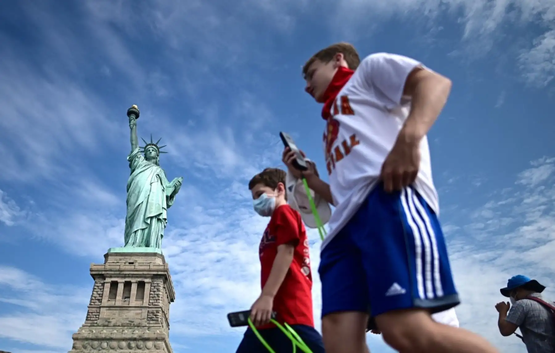 Los turistas que llevan máscaras faciales caminan sobre la Isla de la Libertad reabierta frente a la Estatua de la Libertad el 20 de julio de 2020 en la ciudad de Nueva York. Foto: AFP