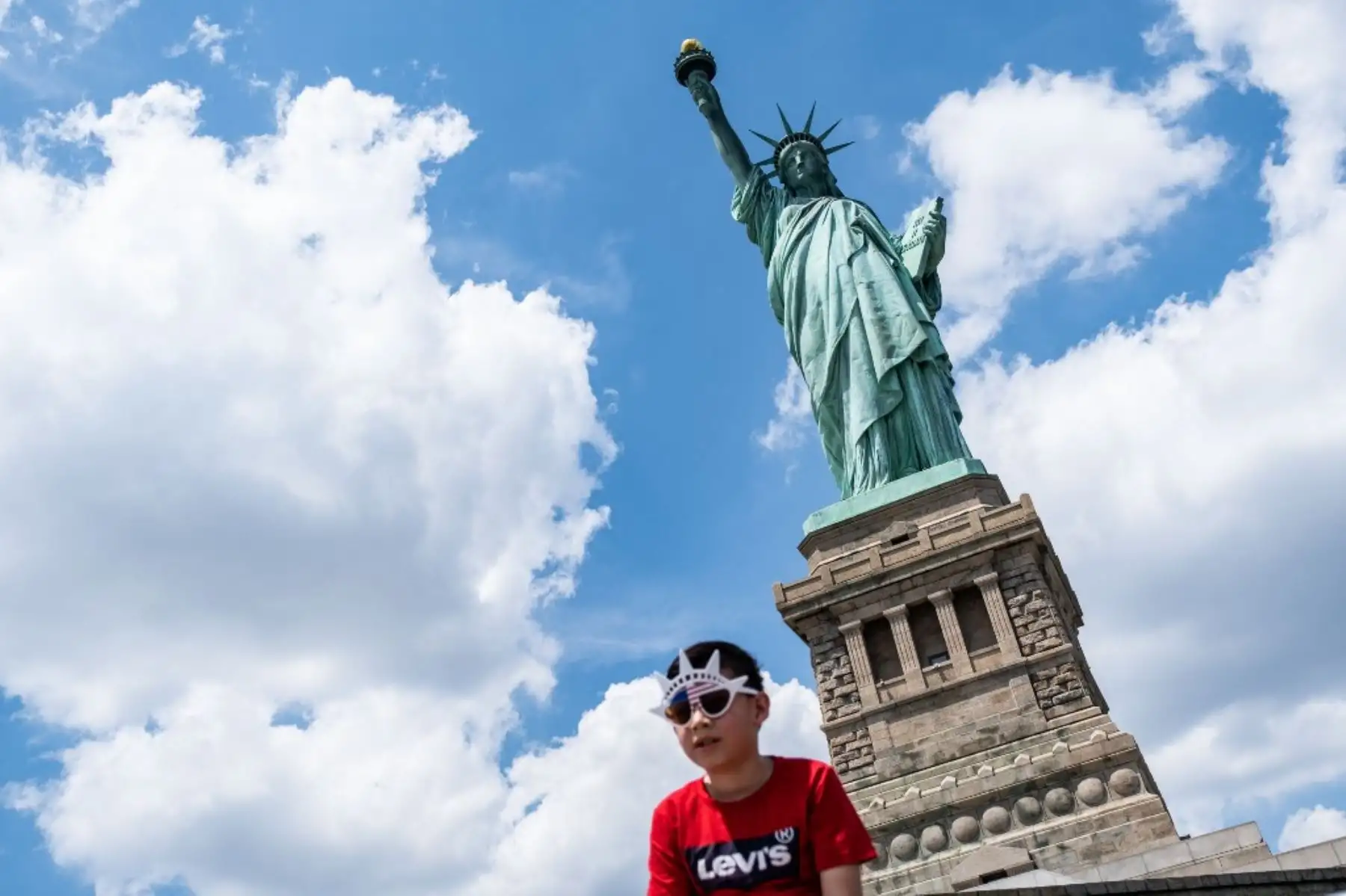 Un niño con gafas de sol se para frente a la Estatua de la Libertad cuando volvió a abrir en la ciudad de Nueva York. Foto: AFP
