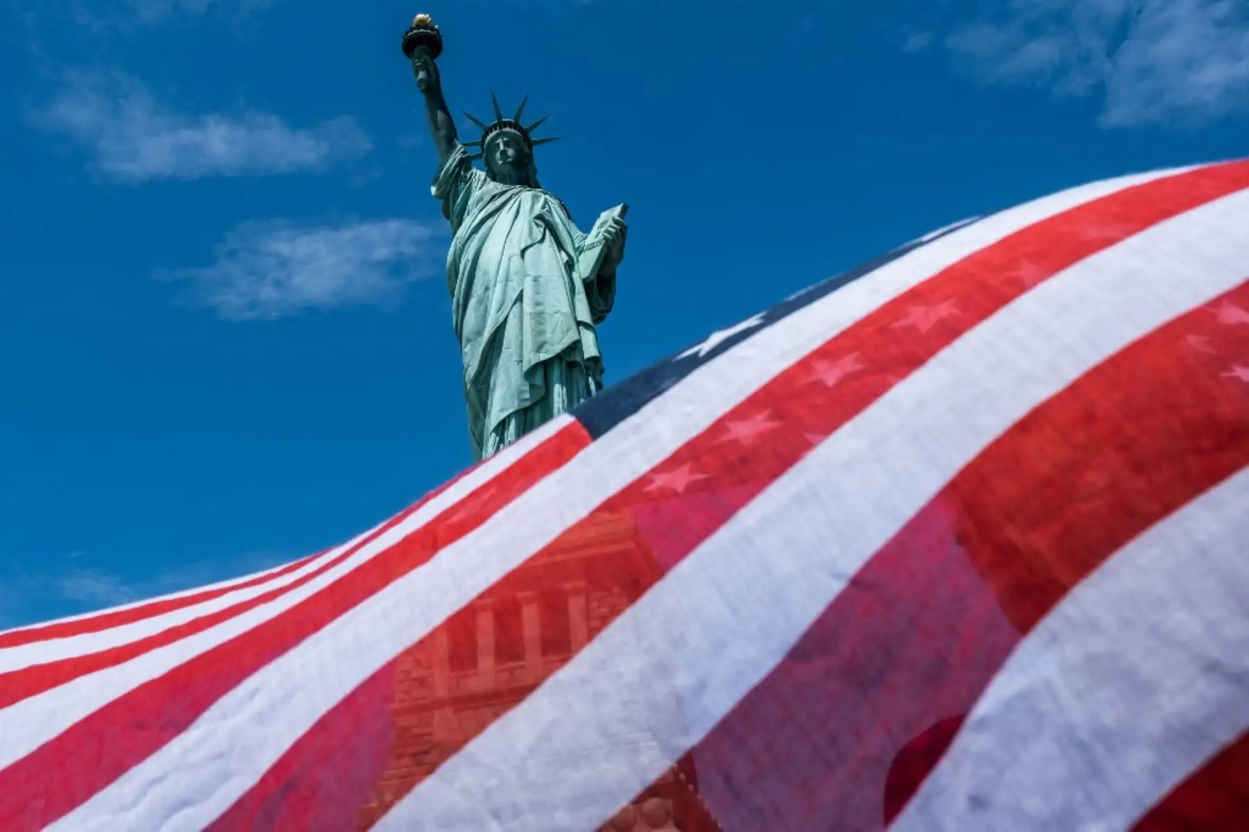 La Estatua de la Libertad se ve sobre una bufanda de bandera estadounidense soplada por el viento en la ciudad de Nueva York. Foto: AFP