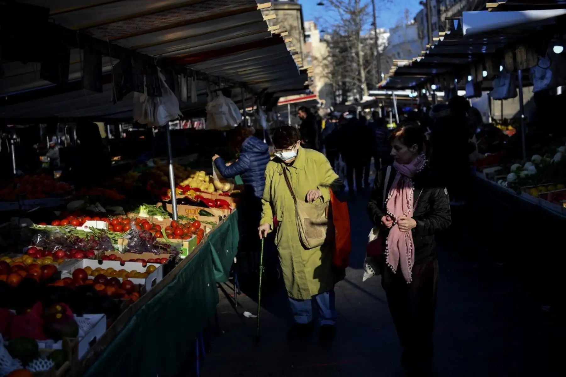 Una mujer con una máscara facial camina por los puestos de comida en un mercado de alimentos en París. Foto: AFP