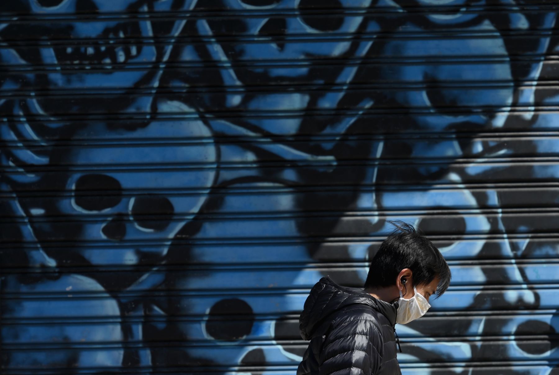 Un hombre con mascarilla pasa junto a un mural en el distrito de Brooklyn de Nueva York, en plena pandemia del coronavirus. Foto: AFP