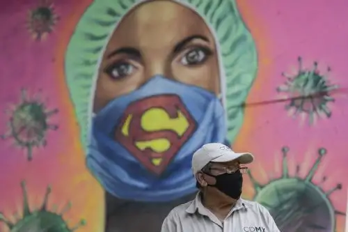 Un jardinero de la ciudad trabaja junto a un mural que muestra a un miembro de la sanidad usando una mascarilla con el símbolo del superhéroe ficticio Supermán, en Ciudad de México, en medio de la nueva pandemia del covid-19. Foto: AFP.