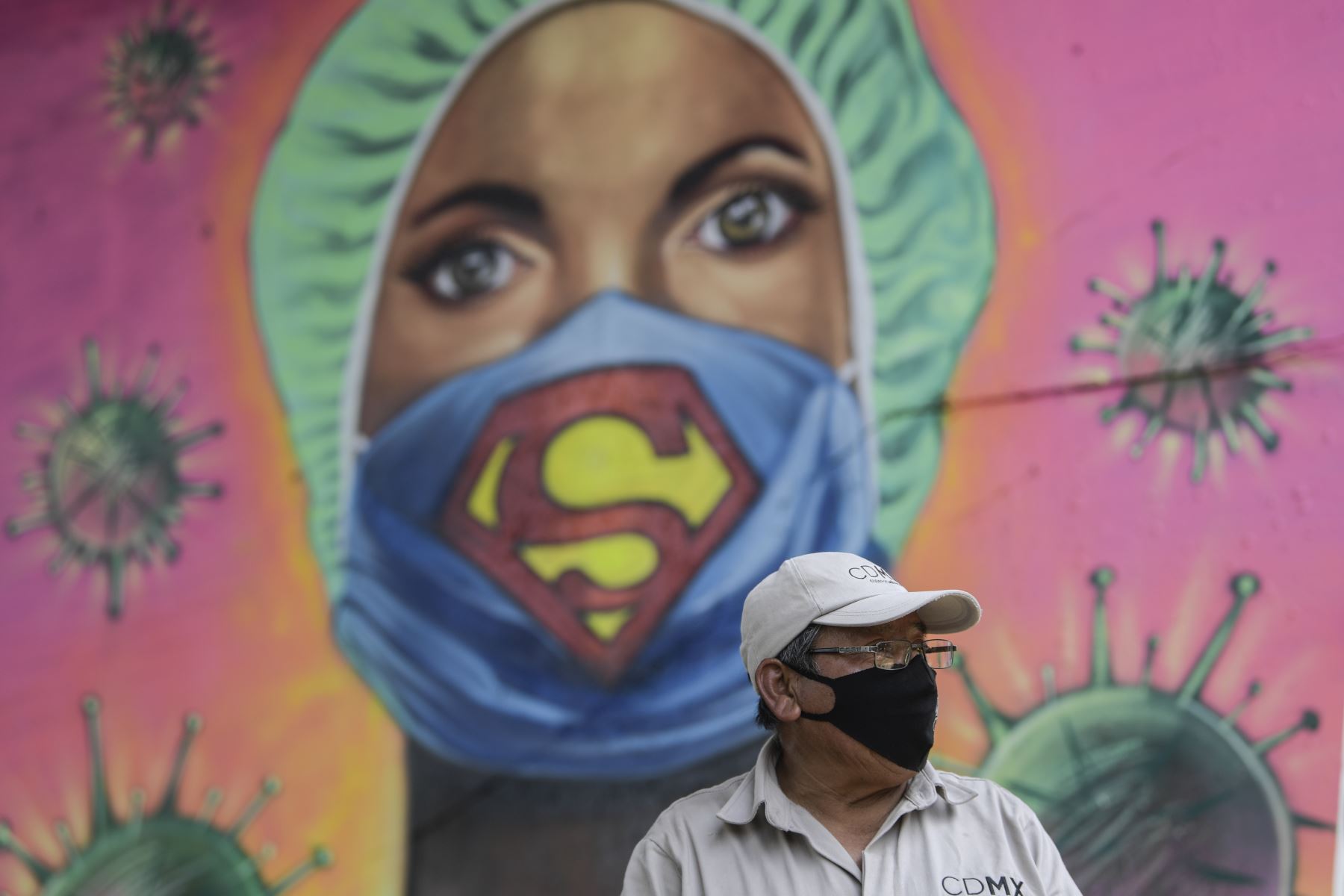 Un jardinero de la ciudad trabaja junto a un mural que muestra a un trabajador de la salud con una máscara facial con el símbolo del superhéroe ficticio "Superman". Foto: AFP