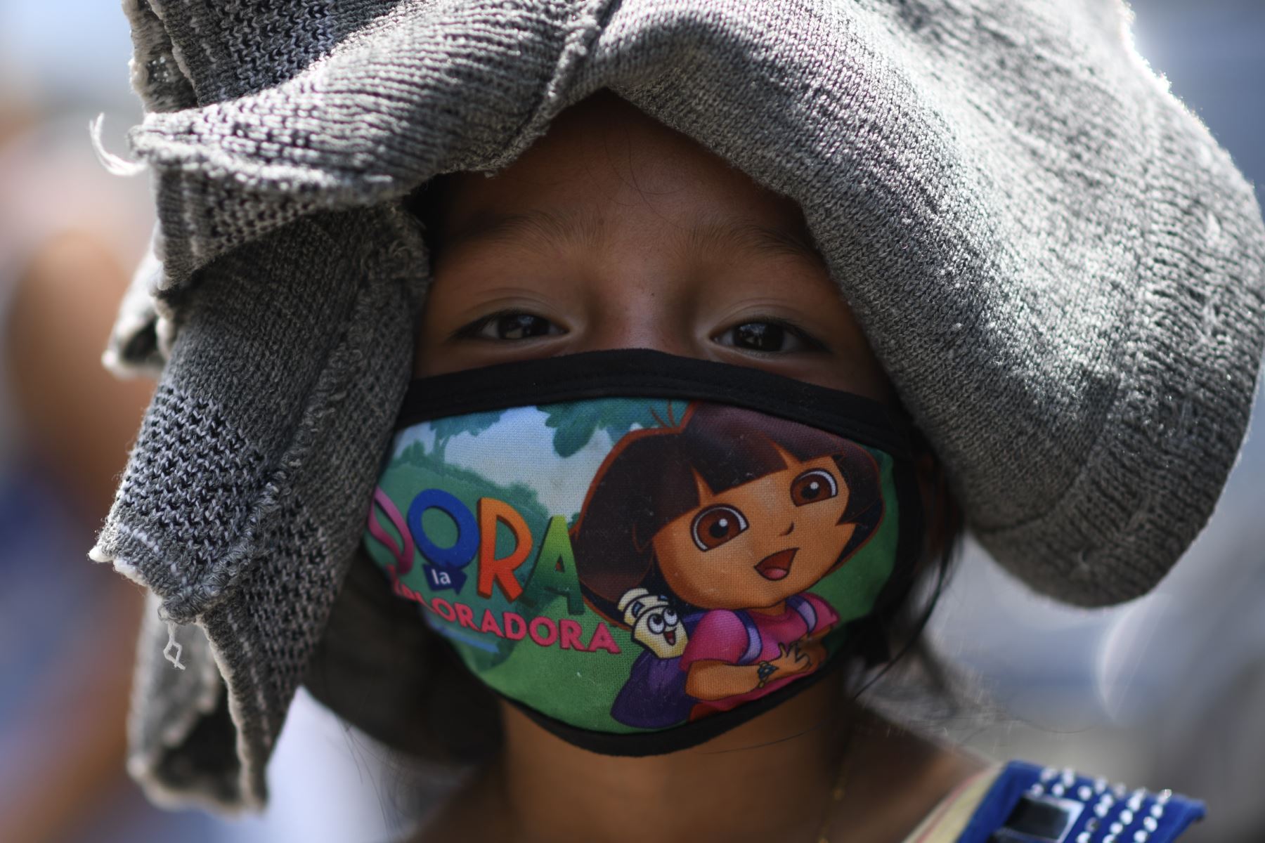 Una niña, cuya familia se vio afectada económicamente por el coronavirus, posa para una foto con un suéter en la cabeza para protegerse del sol, antes de recibir una comida caliente de los trabajadores municipales en el barrio de la Ciudad Peronia, en el municipio de Villa Nueva, a 20 km al sur de la Ciudad de Guatemala. Foto: AFP