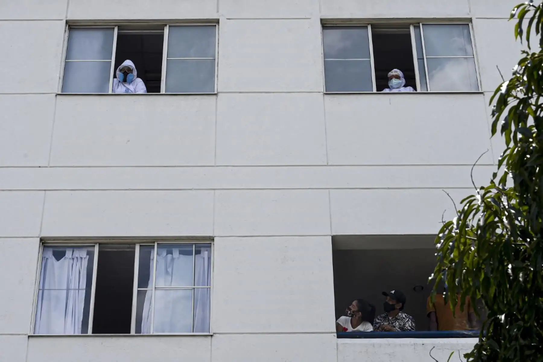 Trabajadores de la salud, pacientes y familiares miran desde las ventanas del hospital mientras una banda de música toca desde afuera en Medellín, Colombia. Foto: AFP