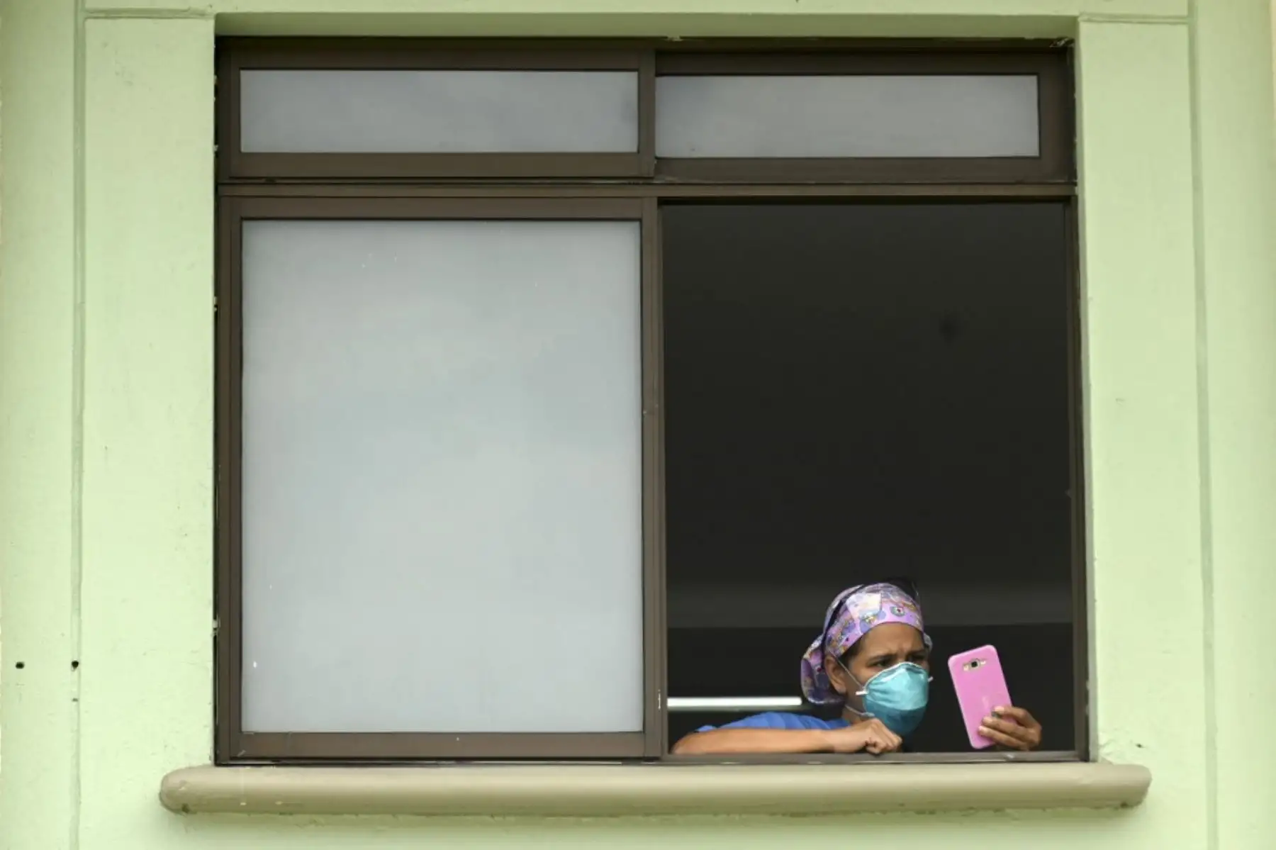Trabajadores de la salud, pacientes y familiares miran desde las ventanas del hospital mientras una banda de música toca desde afuera en Medellín, Colombia. Foto: AFP