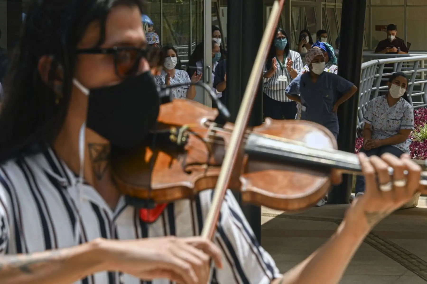 Trabajadores de la salud, pacientes y familiares miran desde las ventanas del hospital mientras una banda de música toca desde afuera en Medellín, Colombia. Foto: AFP