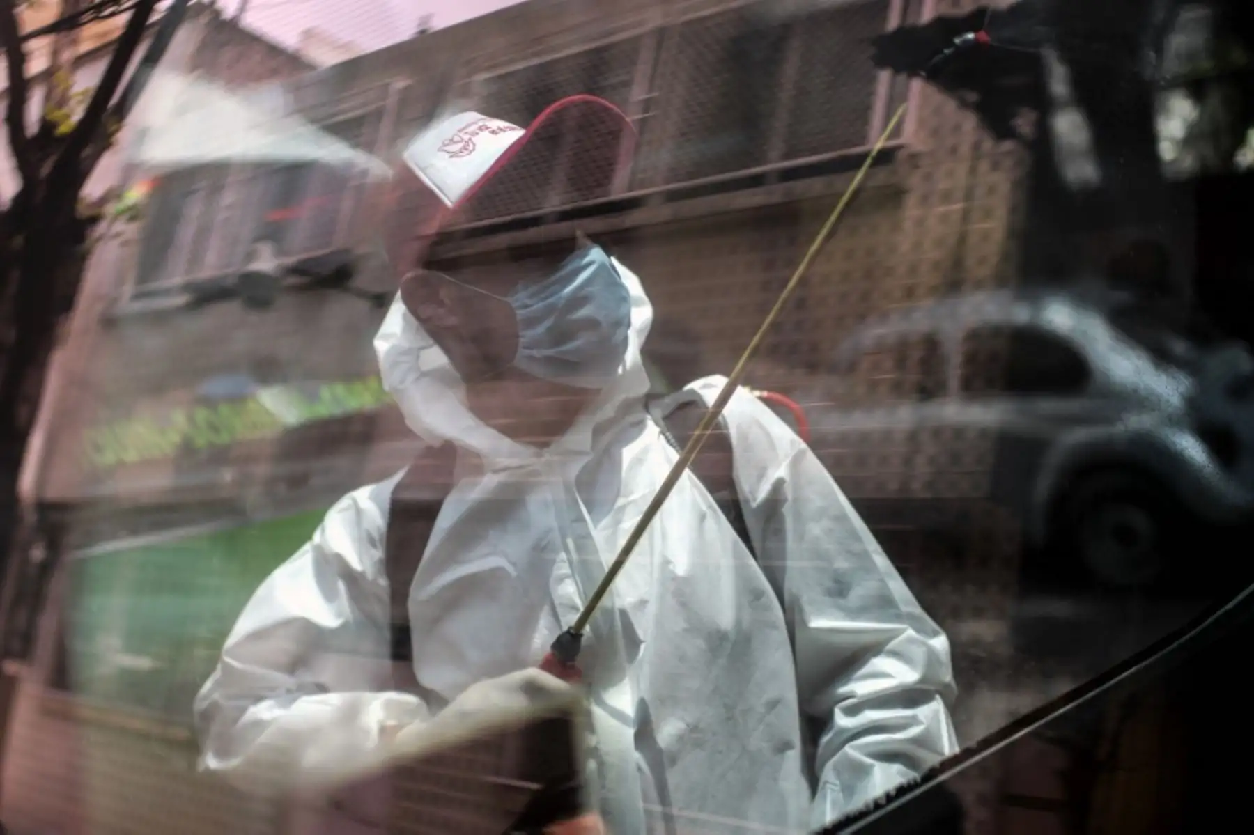 Un trabajador de limpieza con equipo de protección personal se refleja en una ventana mientras desinfecta una camioneta de transporte público en la Ciudad de México. Foto: AFP
