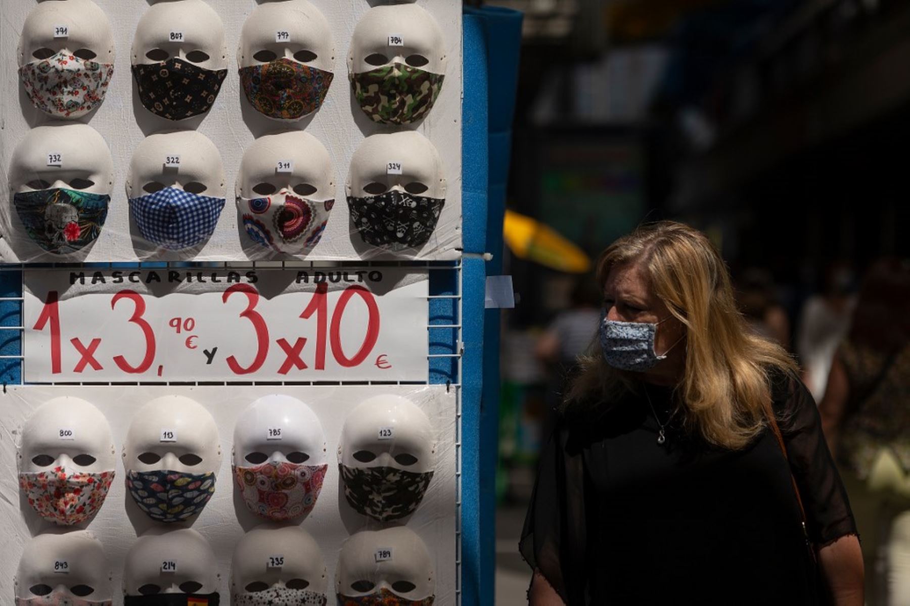 Una mujer con una máscara facial pasa frente a una exhibición de máscaras en venta en una tienda en el centro de Madrid. Foto: AFP