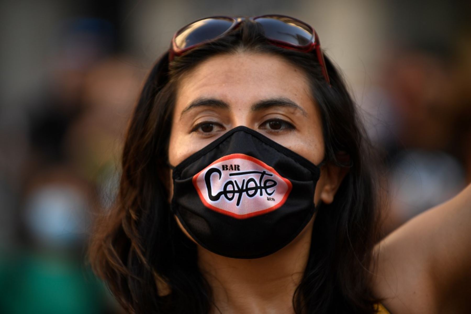 Una mujer con una máscara facial con el logotipo de un bar participa en una manifestación en España. Foto: AFP
