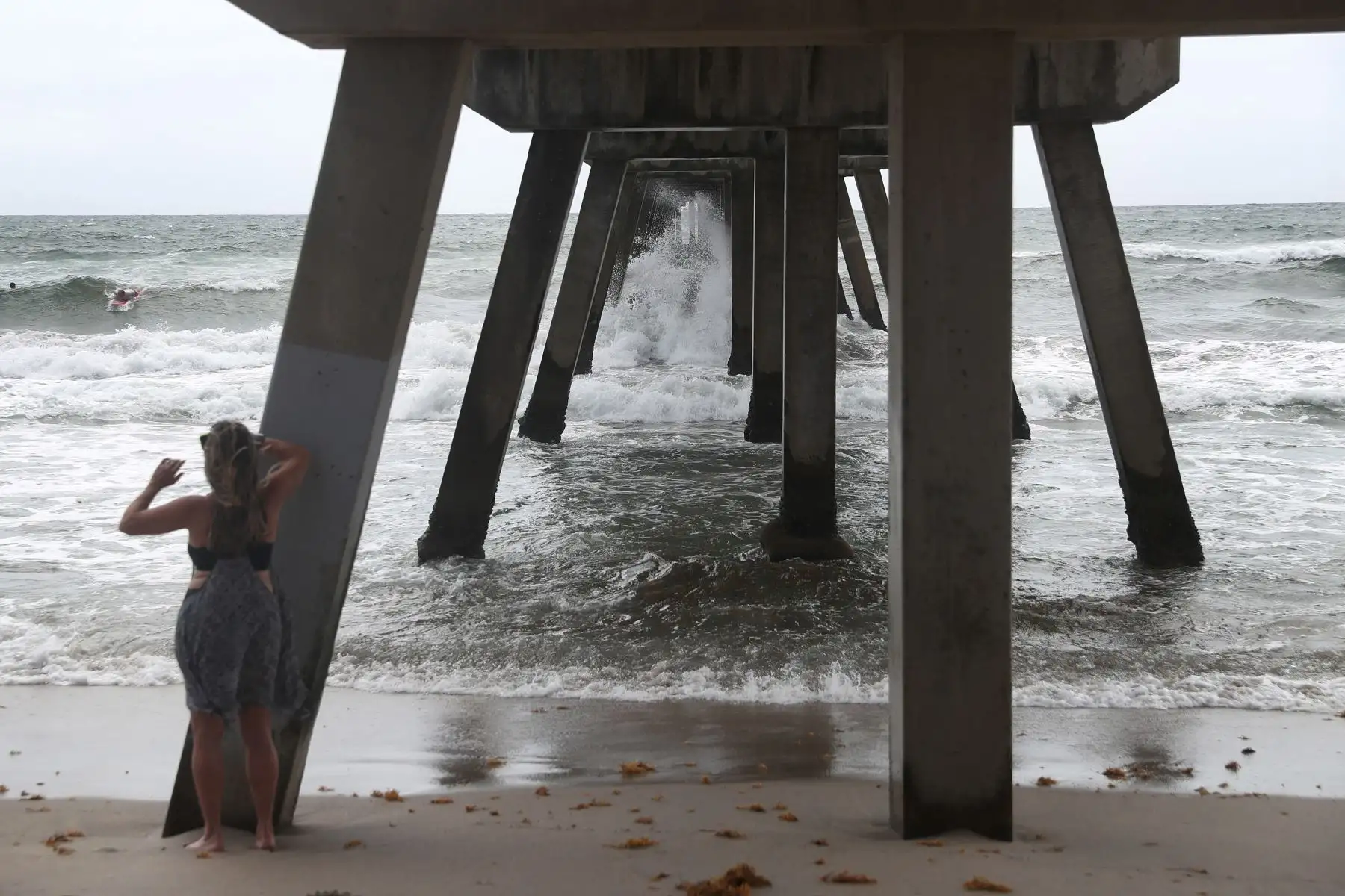 Una mujer filma a los surfistas que practican este deporte por crecida de las olas, en Deerfield Beach, Florida. Foto: AFP