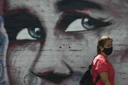 Una mujer usa una mascarilla como medida preventiva contra la propagación del nuevo coronavirus, cuando pasa junto a un mural en Cali, Colombia. Foto: AFP