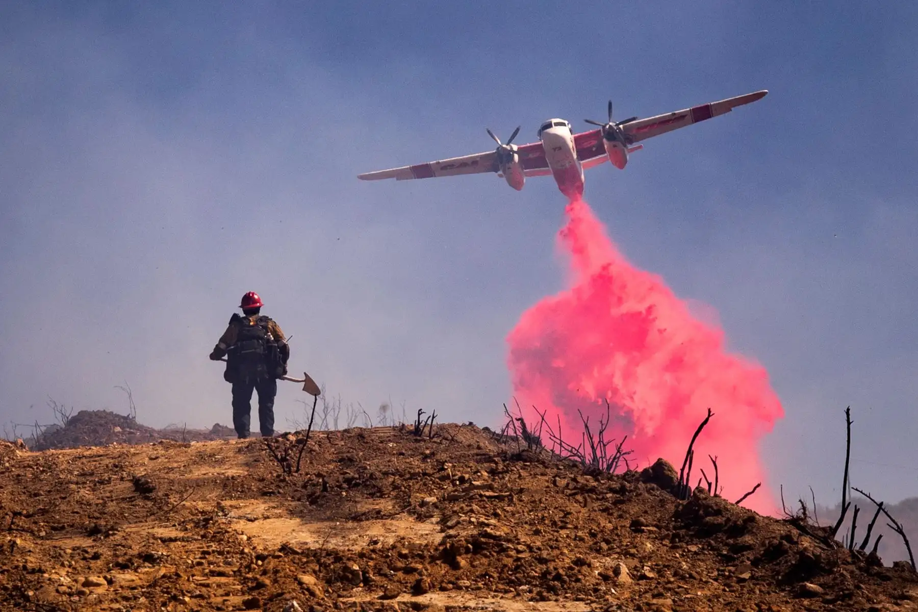 Un avión vuela sobre un bombero y arroja retardante de fuego en Elsmere Fire cerca de Santa Clarita, California, EE. UU. Según los últimos informes de los medios, el incendio ha quemado 130 acres.

Foto: EFE