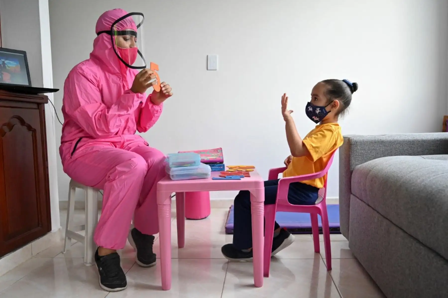 Una maestra que usa un traje de bioseguridad como medida preventiva contra la propagación del nuevo coronavirus, covid-19, da una clase a una niña en su casa en Cali, Colombia. Foto: AFP