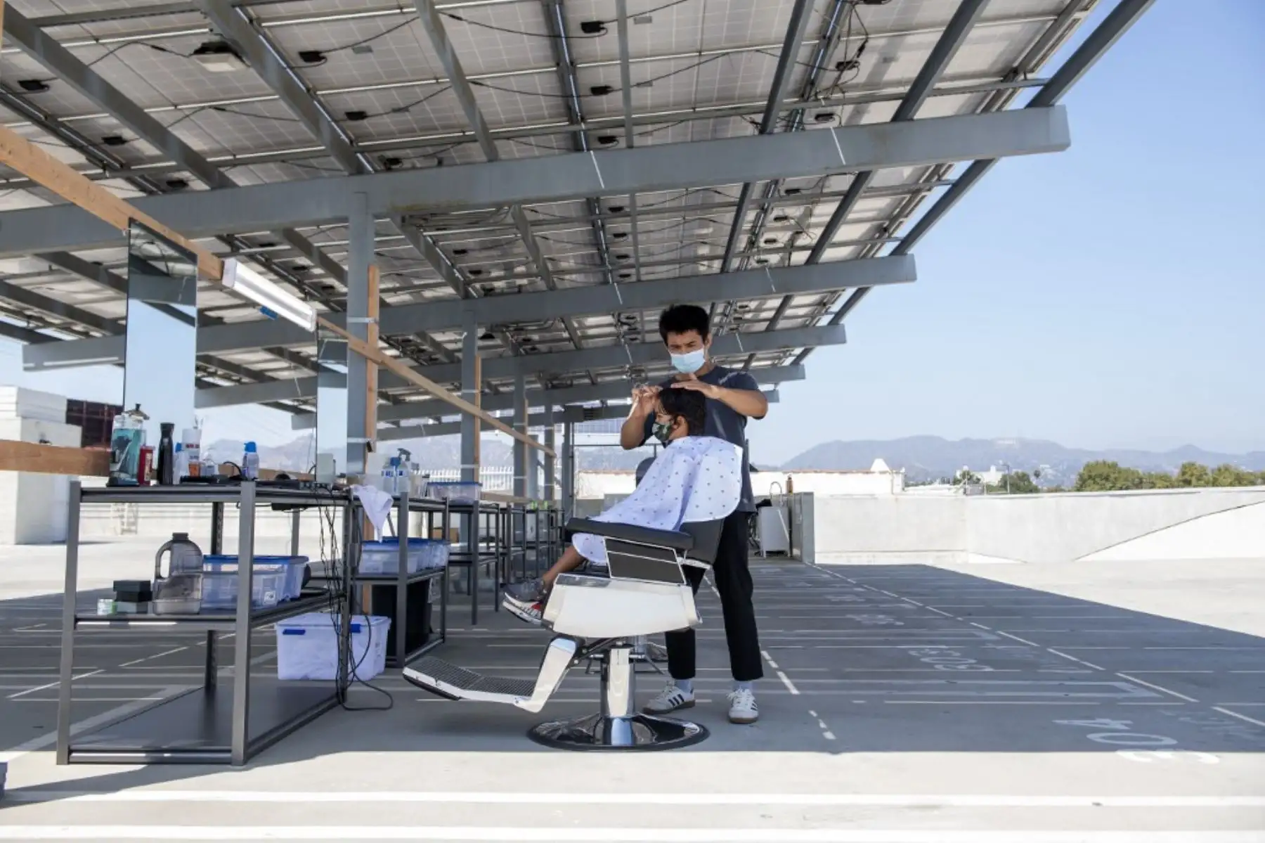 Un estilista corta el cabello de un joven cliente en un estacionamiento de la azotea en medio de la nueva pandemia de coronavirus en Los Ángeles, California. Foto: AFP