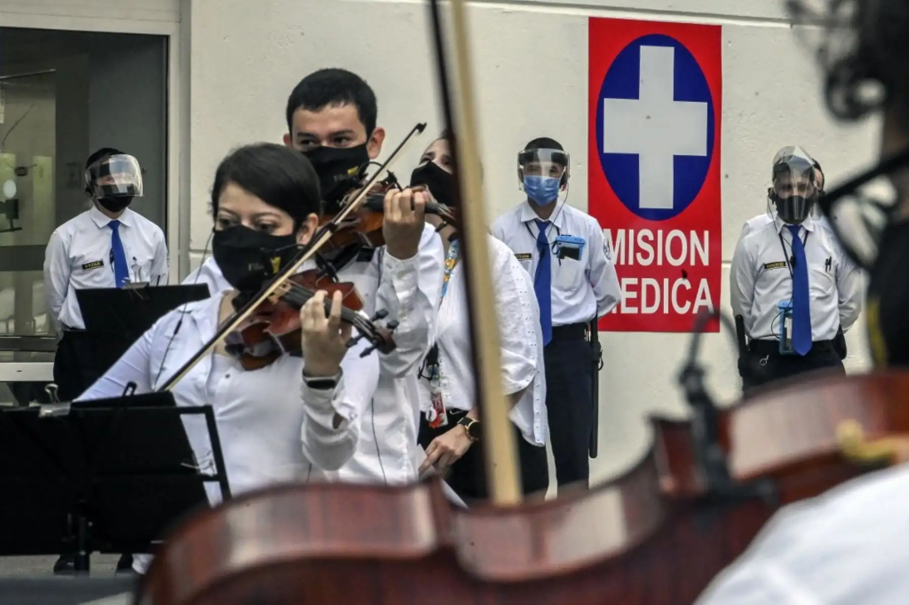 Trabajadores de la salud, pacientes y familiares miran a músicos de la Orquesta Filarmónica de Medellín tocando frente a un hospital, en medio de la pandemia covid-19, en Medellín. Foto: AFP