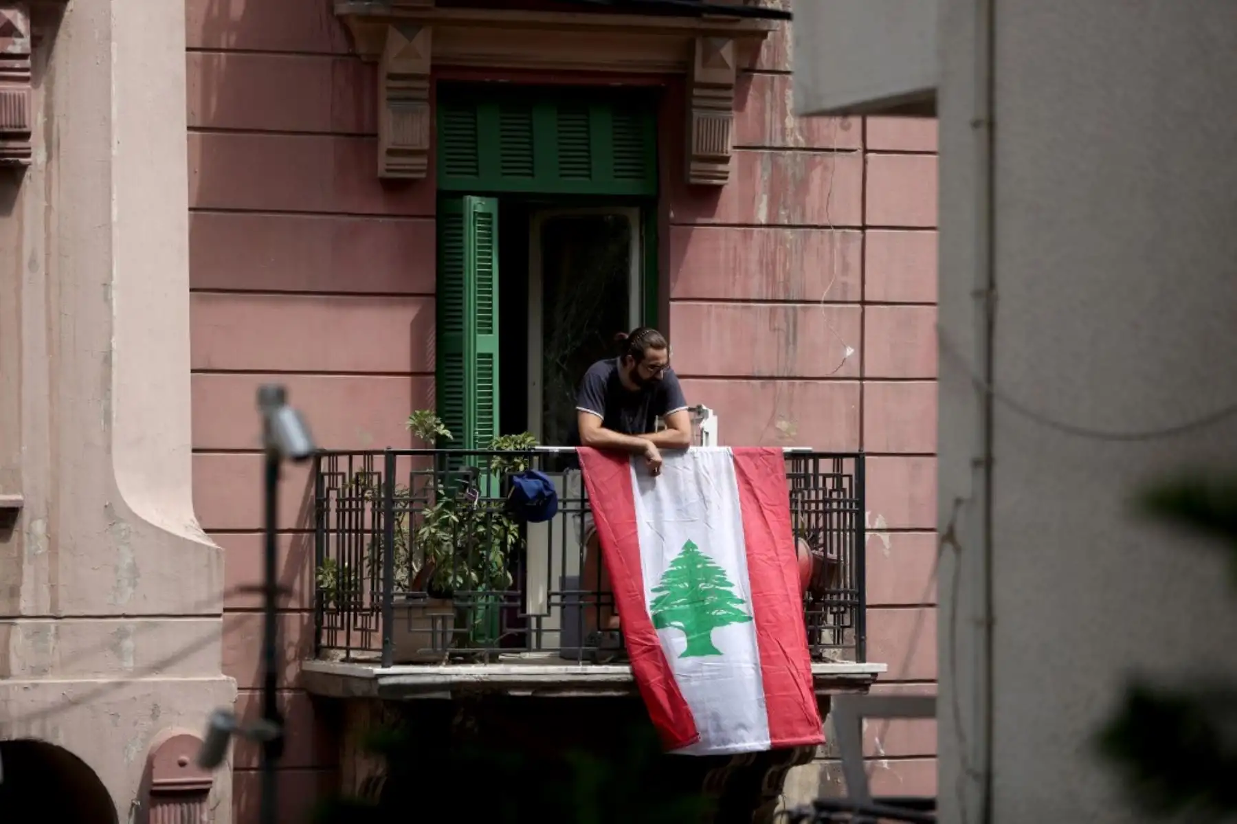 Un hombre se inclina sobre una bandera libanesa que cuelga de este balcón en el vecindario Mar Mikhal de Beirut el 7 de agosto de 2020, tres días después de una explosión masiva en el puerto de la capital libanesa. Foto: AFP