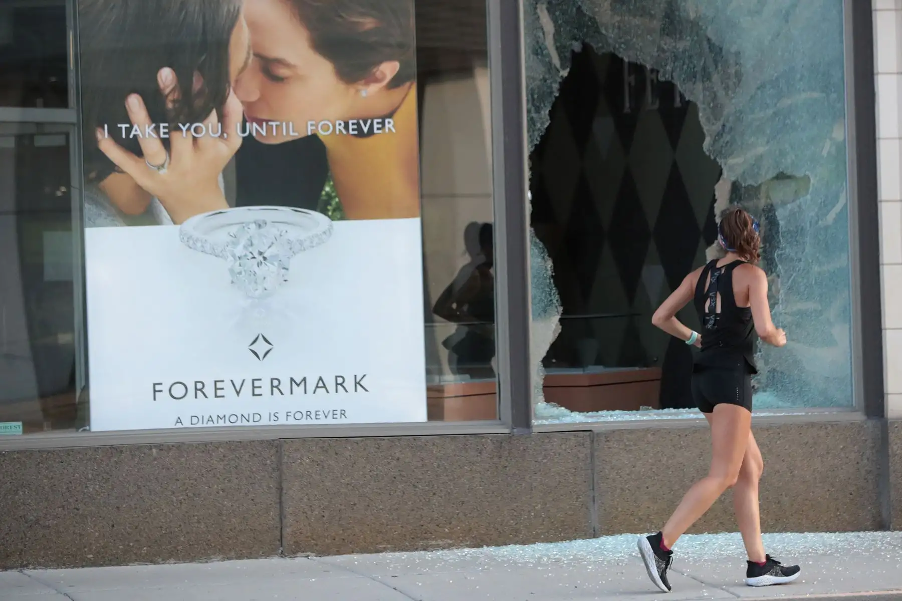 Una  mujer que realiza deporte pasa junto a la ventana de una tienda saqueada durante una noche de vandalismo, en Chicago, Illinois. Foto: AFP