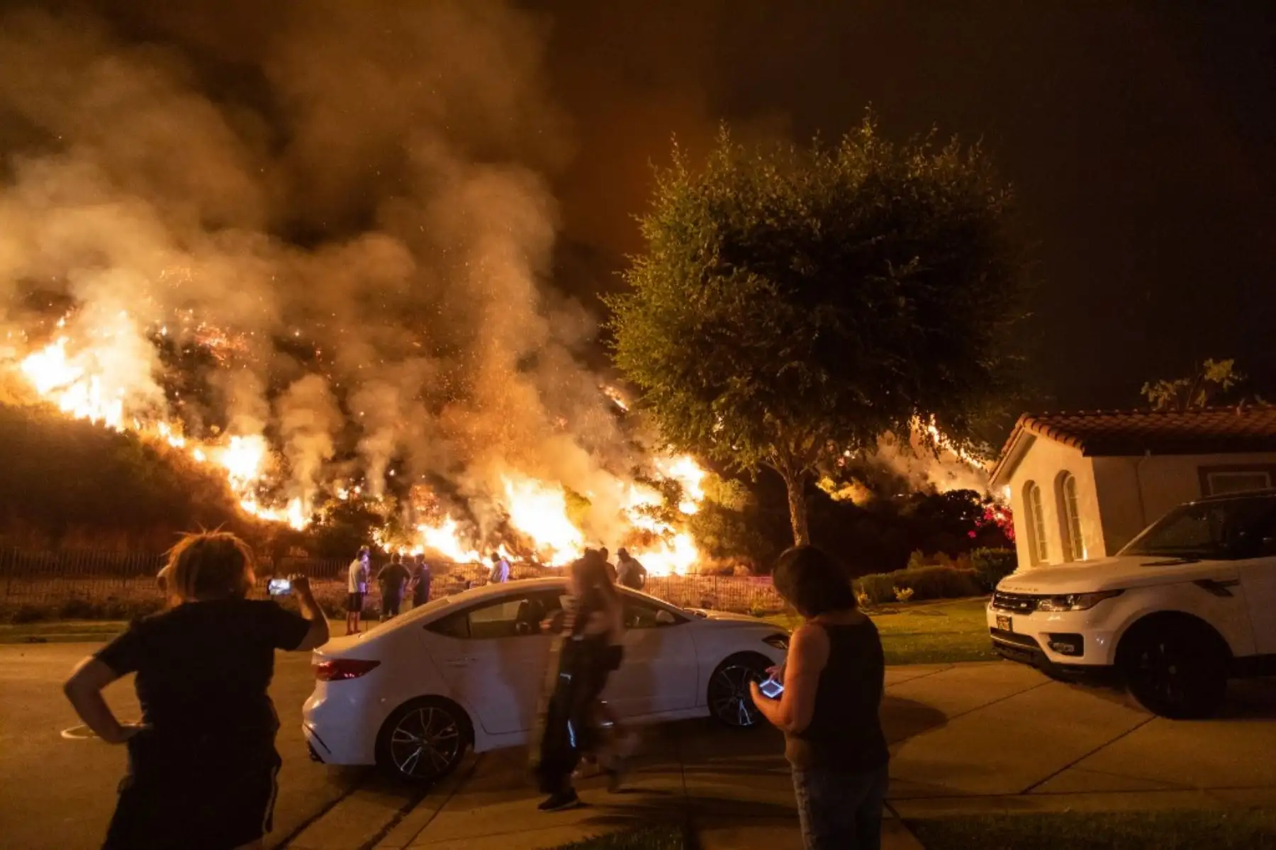 La gente se para junto a las llamas que se elevan desde el incendio del rancho en las montañas de San Gabriel sobre Azusa, a 25 millas al este de Los Ángeles, California. Foto: AFP