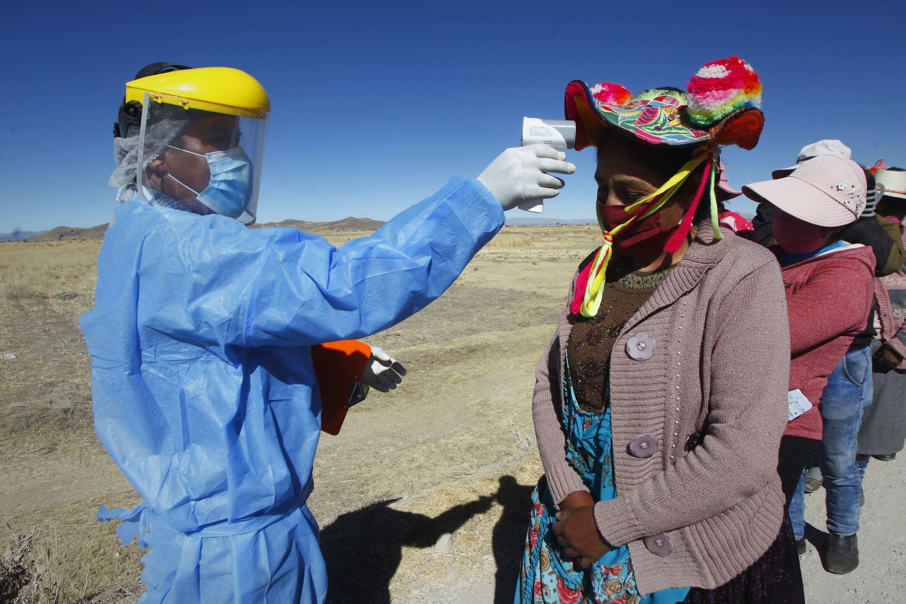 Un hombre toma la temperatura a mujeres de las comunidades altoandinas quechuas antes de ingresar a una feria rural en la localidad de Coata, en Puno. Foto: EFE