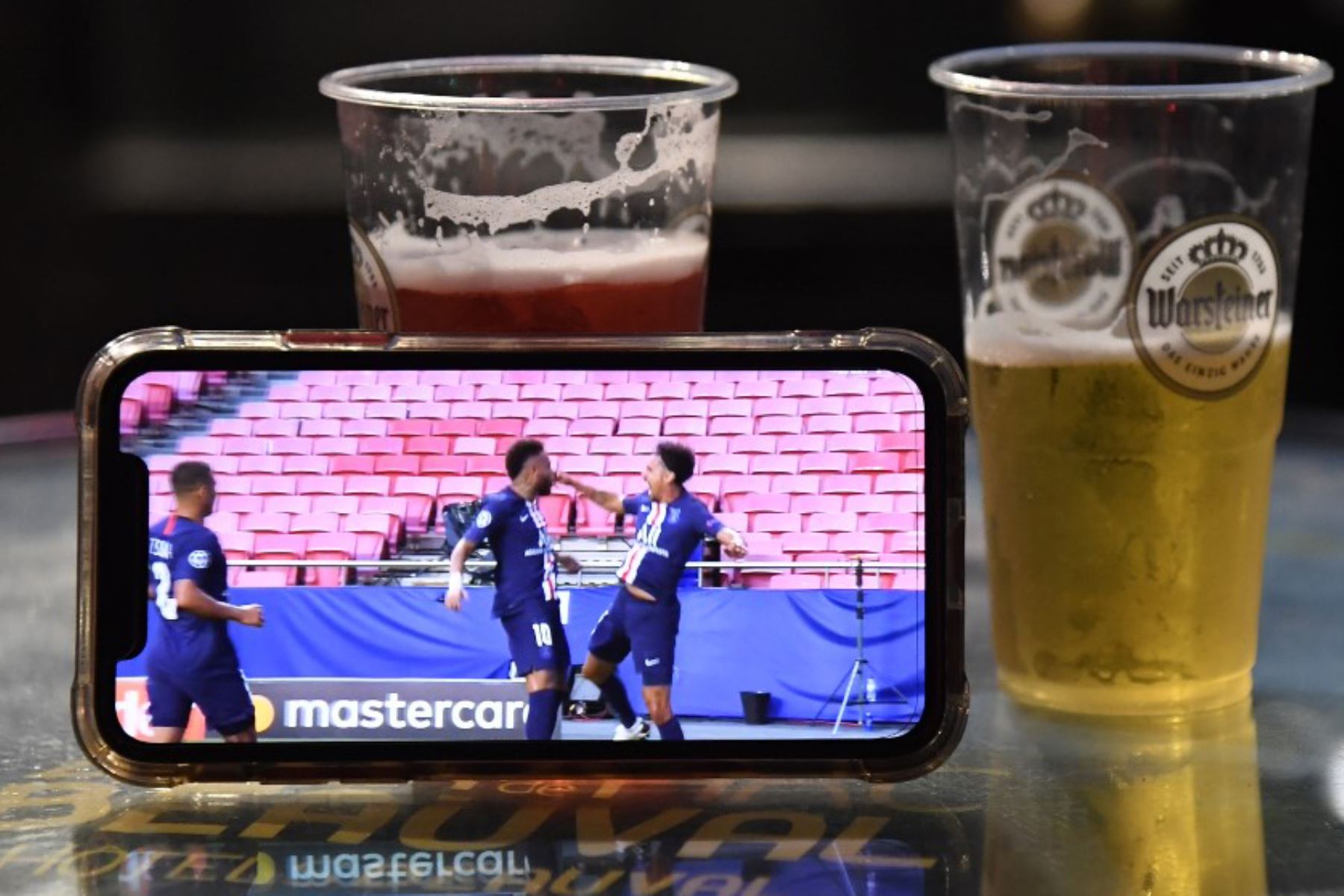 Un teléfono inteligente apoyado sobre vasos de cerveza en París muestra una transmisión del partido de fútbol de semifinales de la Liga de Campeones de la UEFA entre Leipzig y Paris Saint-Germain, jugado en Lisboa.

Foto: AFP