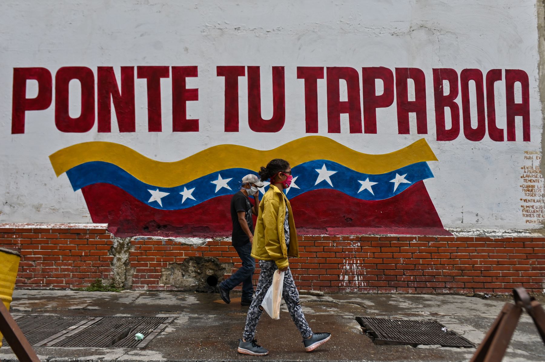 Personas con mascarillas pasan frente a una pared que dice “Ponte la mascarilla” en el centro de Caracas. Foto: AFP