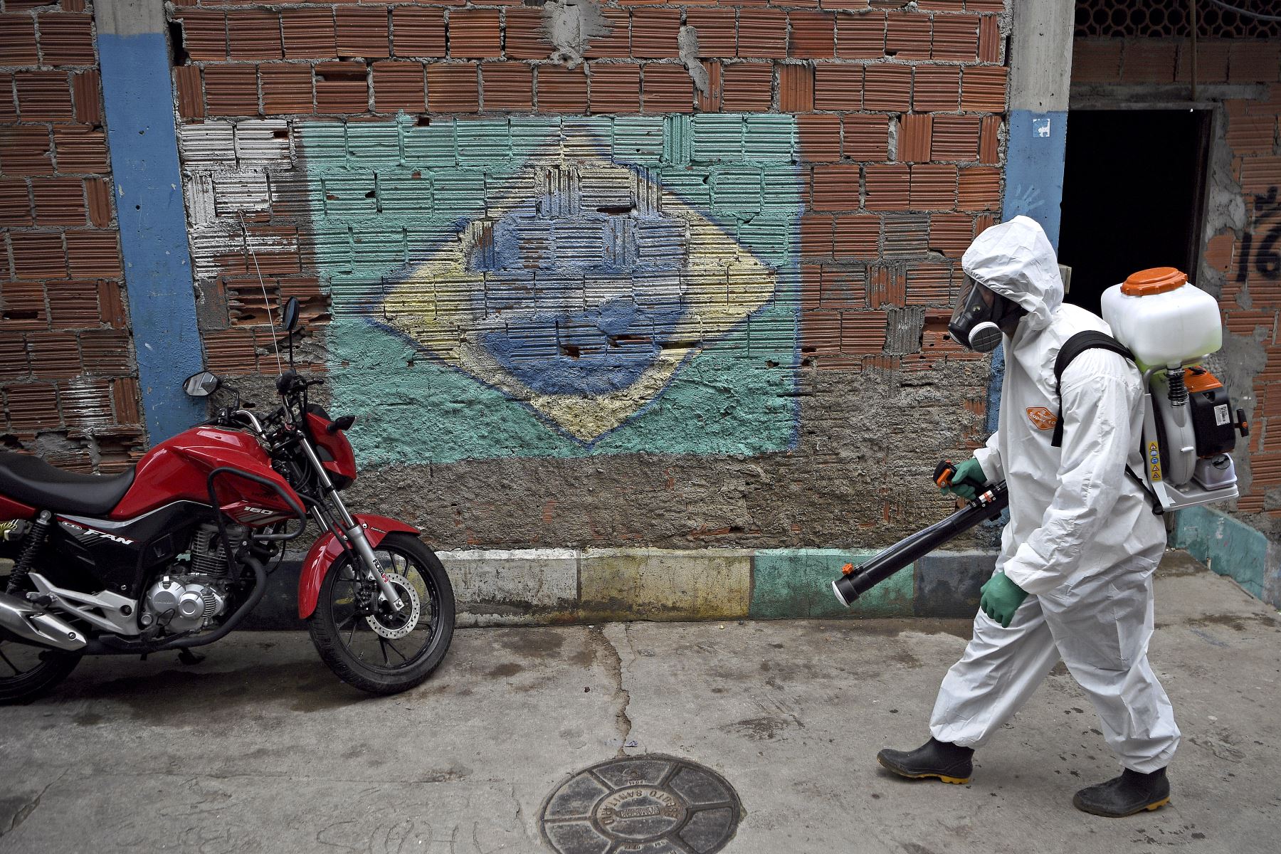 En esta foto de archivo tomada el 18 de abril de 2020, un voluntario pasa junto a un mural que representa una bandera brasileña mientras desinfecta un área en la favela de Babilonia, en Río de Janeiro, Brasil. Foto: AFP