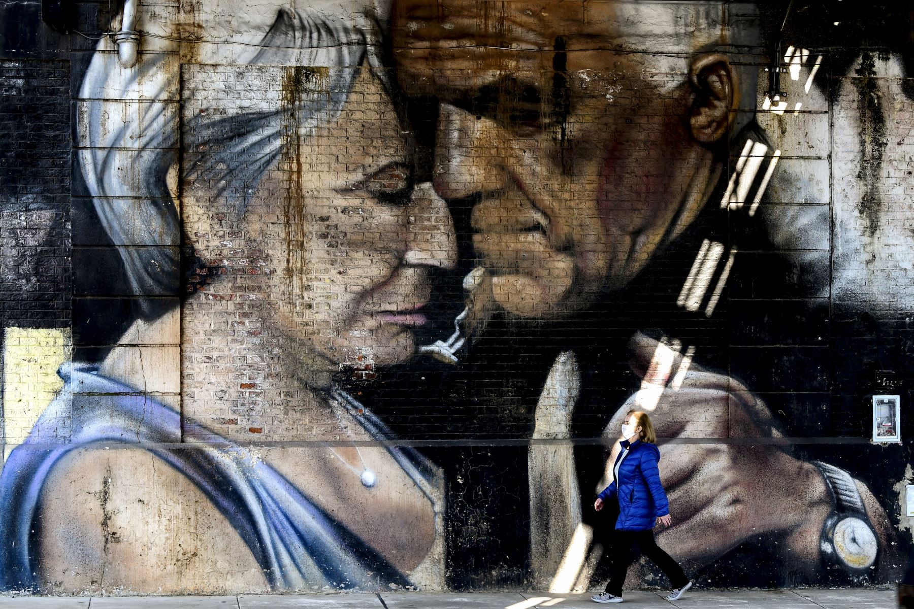 Una mujer con mascarilla camina frente a un mural con la imagen de una pareja bailando tango, en Buenos Aires, Argentina. Foto: AFP