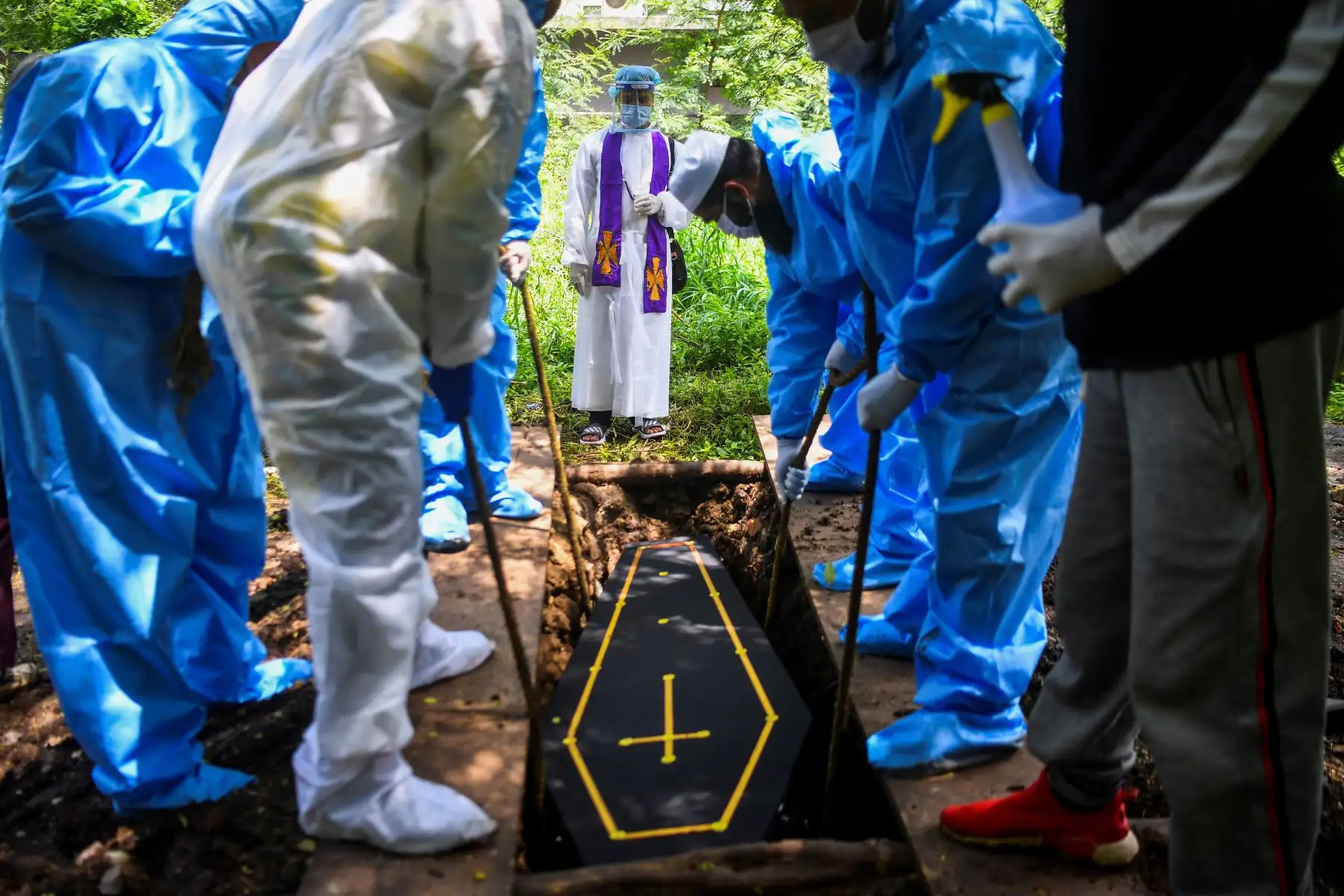 Un pastor ofrece la bendición mientras un grupo de cargadores baja el ataúd de una víctima del coronavirus. Foto: AFP