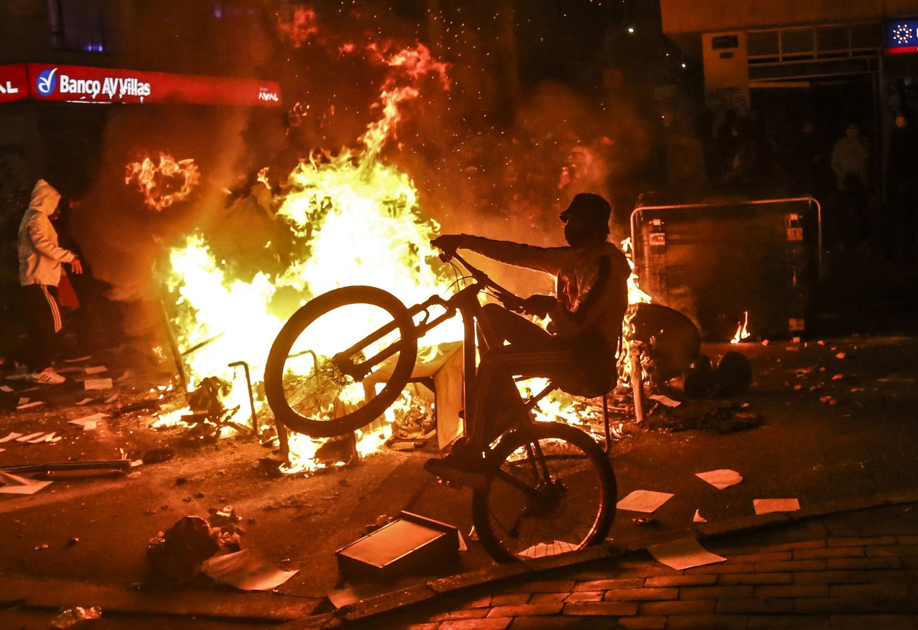 Un manifestante monta una bicicleta en una barricada incendiada durante los enfrentamientos con la policía antidisturbios que estallaron durante una protesta contra la muerte de un abogado bajo custodia policial, en Bogotá. Foto: AFP