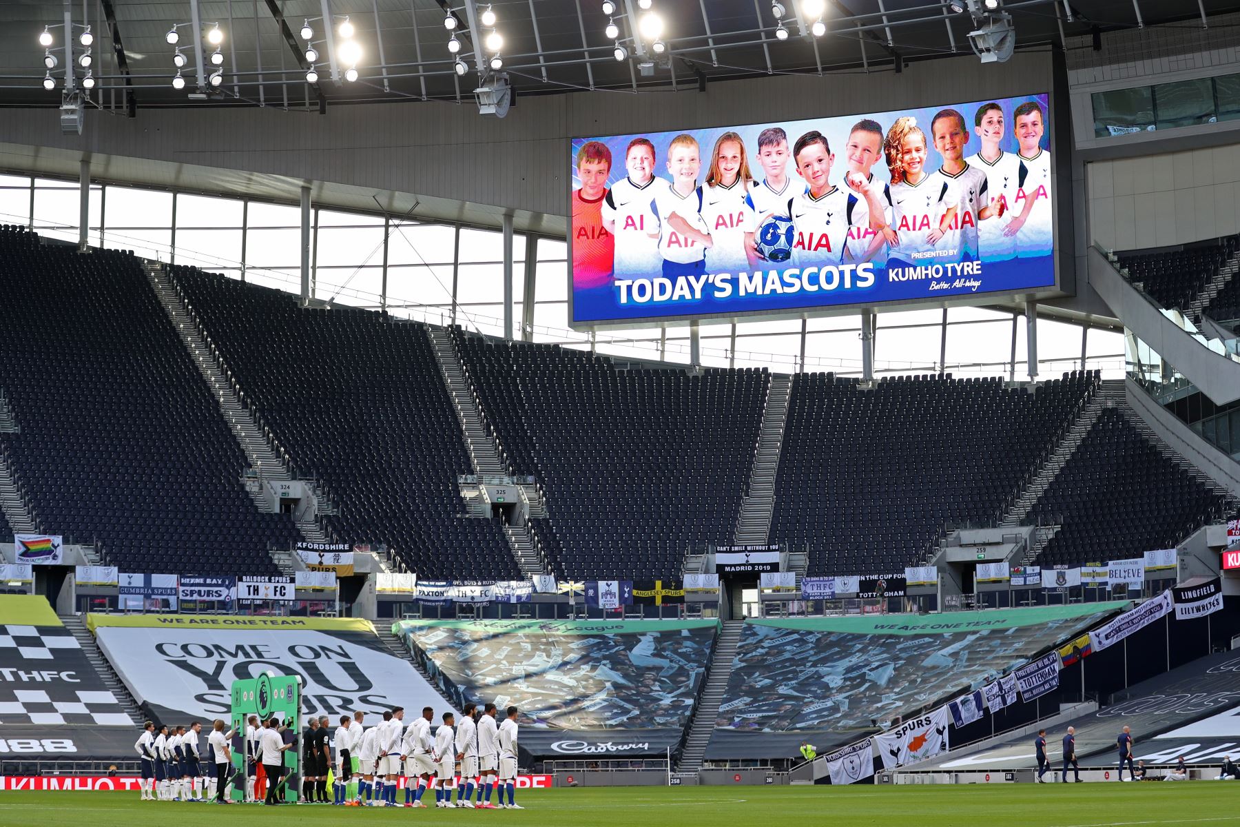 Los jugadores se alinean mientras los niños aparecen de forma virtual en la pantalla gigante, antes del partido de fútbol de la Premier League. Foto: AFP