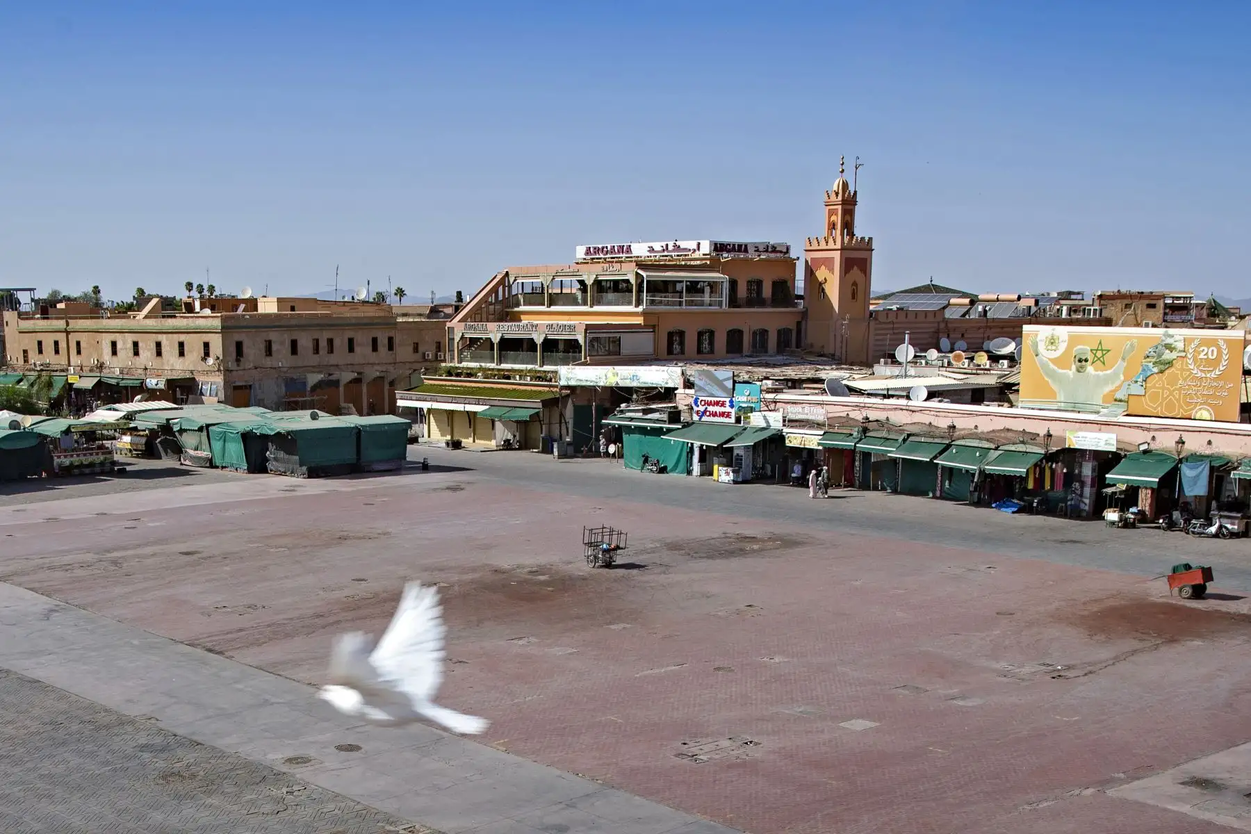 Algunas personas caminan por puestos en su mayoría cerrados en la plaza Jemaa el-Fna en la ciudad marroquí de Marrakech, actualmente vacía de sus multitudes habituales debido a la pandemia de Covid-19. Foto: AFP