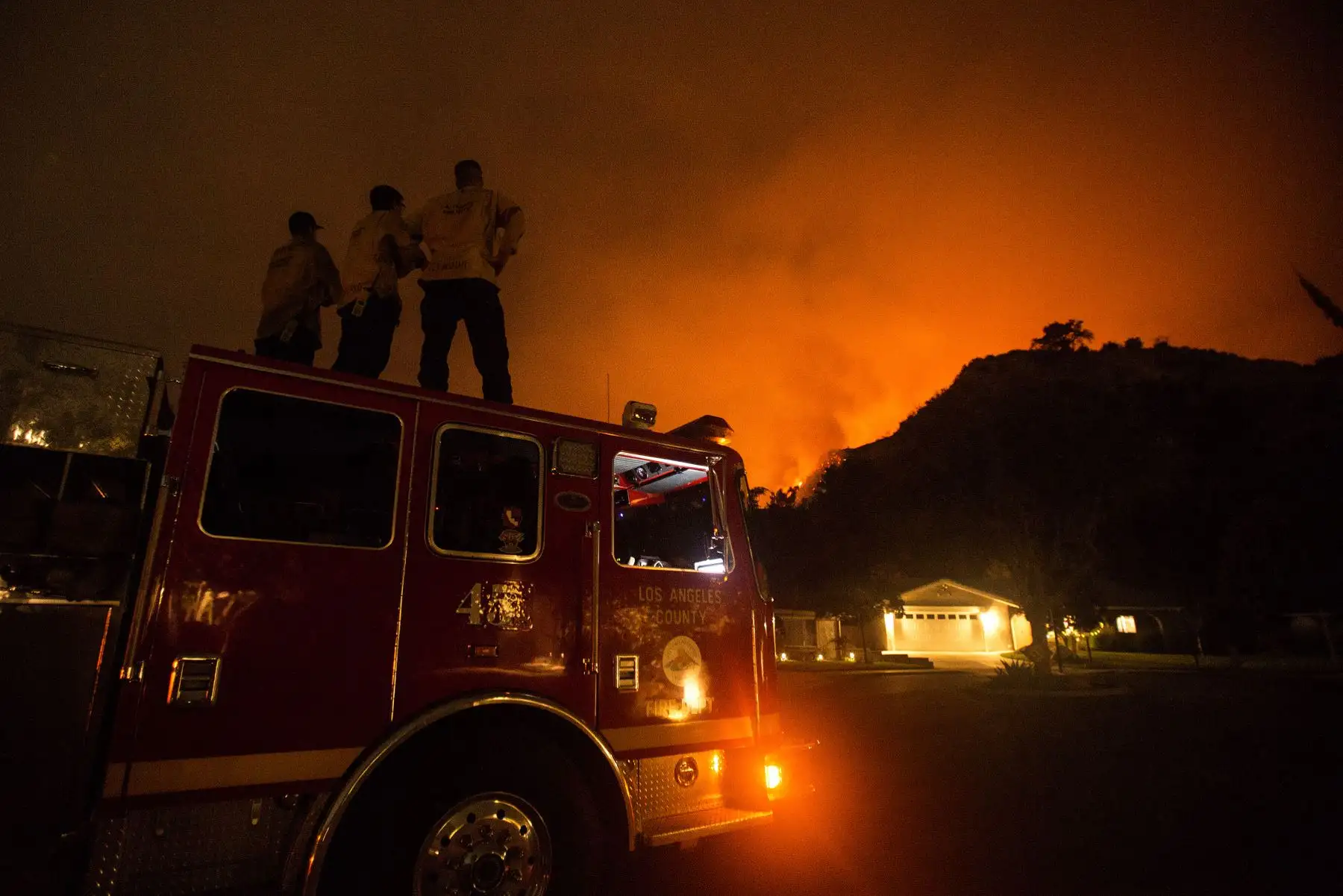 Los bomberos observan cómo arden las laderas detrás de las casas en Monrovia, California. Foto: AFP