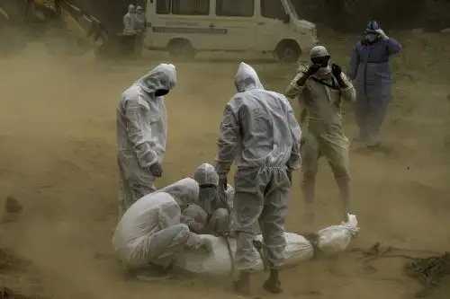 En esta fotografía de archivo tomada el 10 de mayo de 2020, los familiares que usan equipo de protección atan el cadáver de una víctima que murió por el covid-19 antes de un entierro en un cementerio en Nueva Delhi. Foto: AFP
