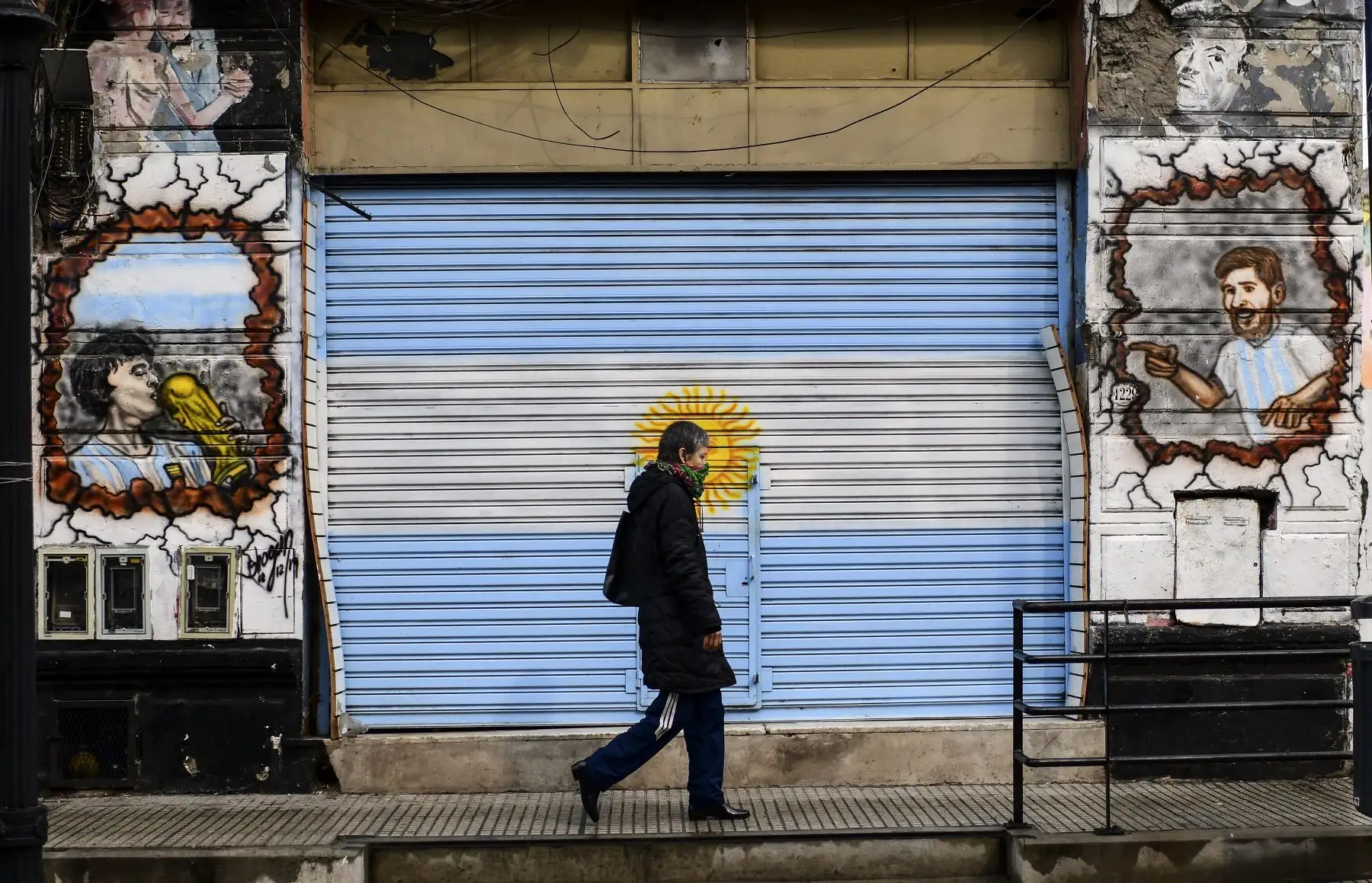 Una mujer con un cubrebocas camina junto a un mural con las imágenes de la estrella del fútbol argentino Lionel Messi y la ex leyenda del fútbol argentino Diego Maradona en el barrio de La Boca, Buenos Aires. Foto: AFP