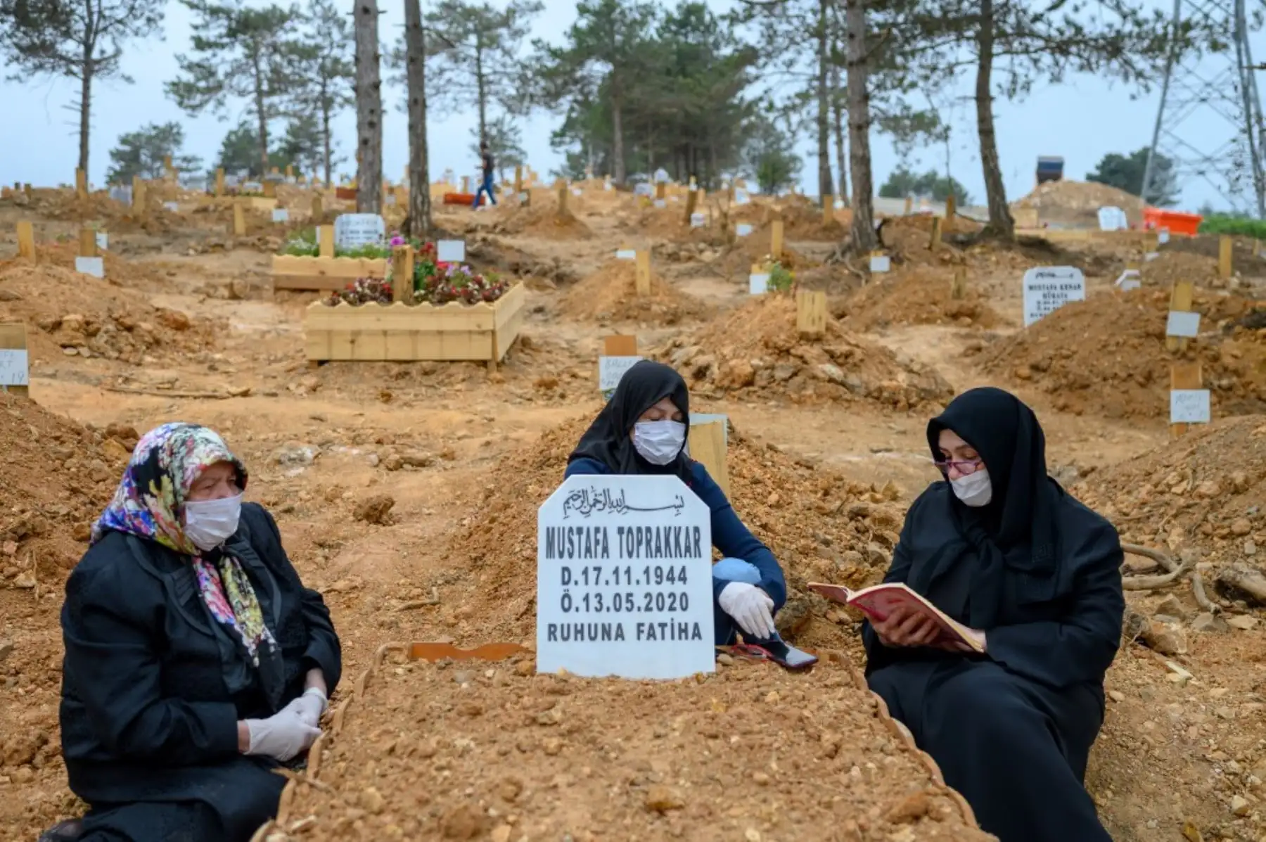 Mujeres con máscaras protectoras rezan en un cementerio junto a la tumba de un familiar que falleció de covid-19, en Estambul. Foto: AFP